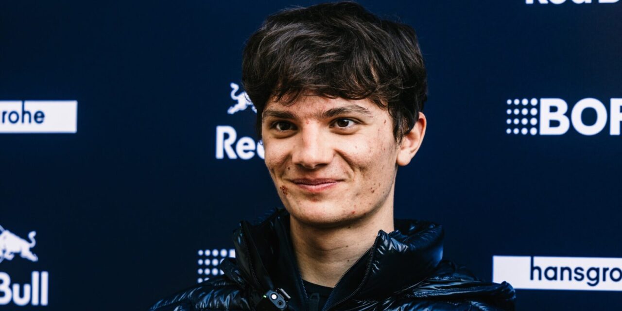Male cyclist smiling at camera during press conference with sponsor backdrop