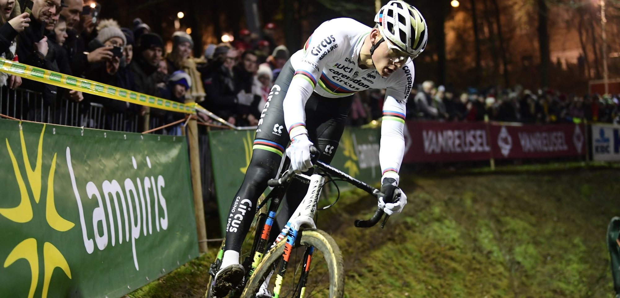 Cyclocross racer in world champion rainbow jersey navigating muddy corner at night race